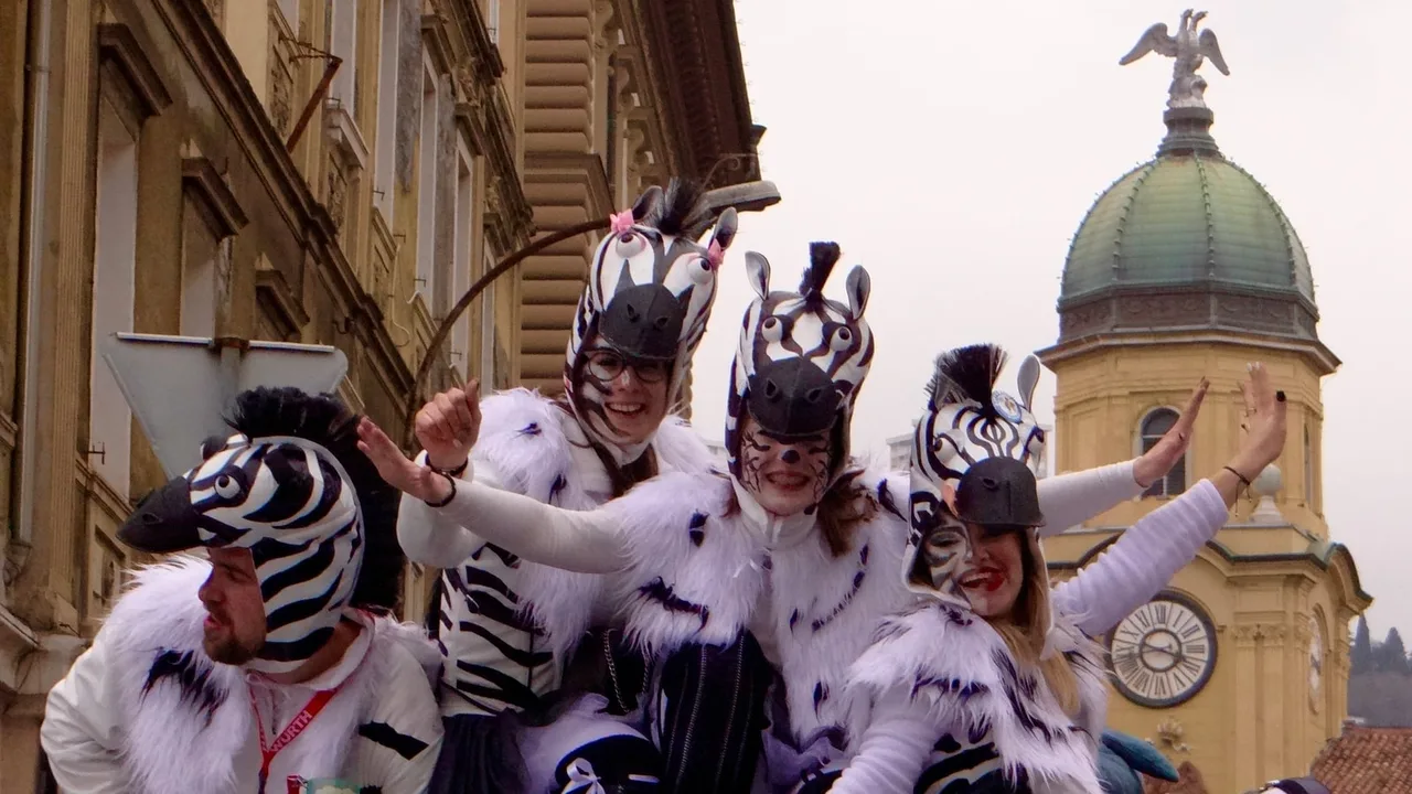 Carnival group dressed as zebras waving from a float in Rijeka, with the green dome of the City Tower behind them