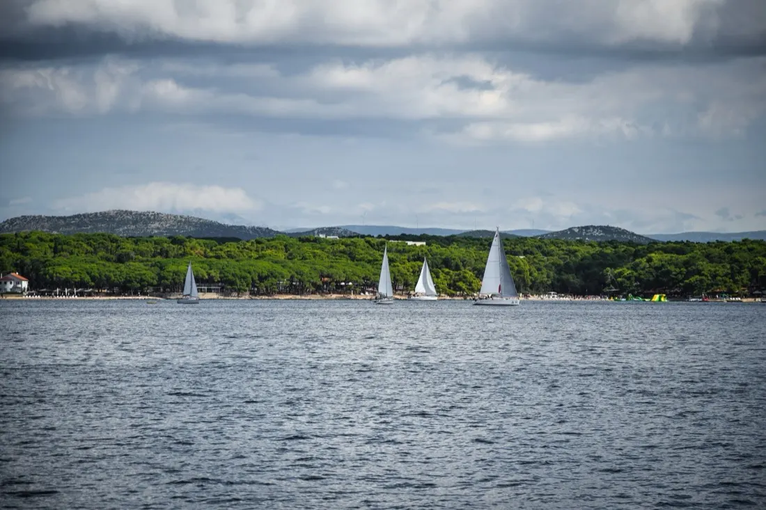 A yacht under sail on a calm Adriatic stretch with low islands on the horizon