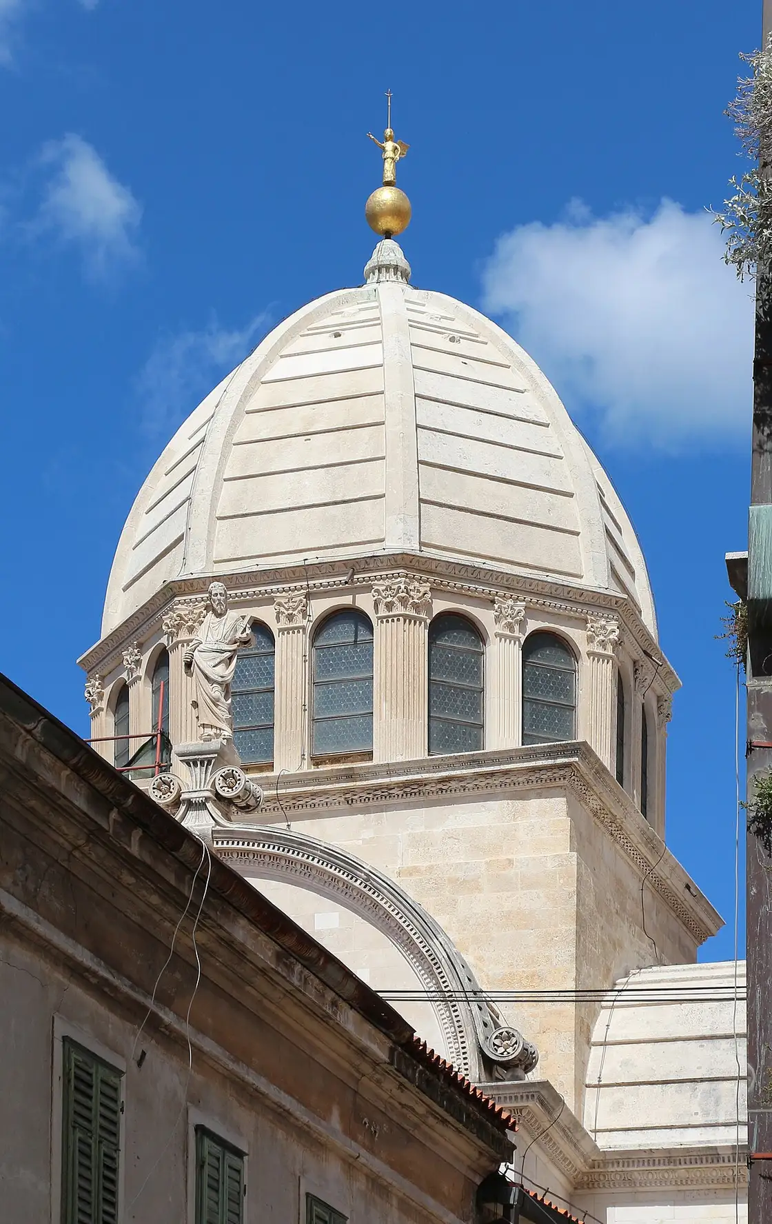 Close view of the octagonal drum and ribbed stone dome of the cathedral of St James in Šibenik, with a carved statue