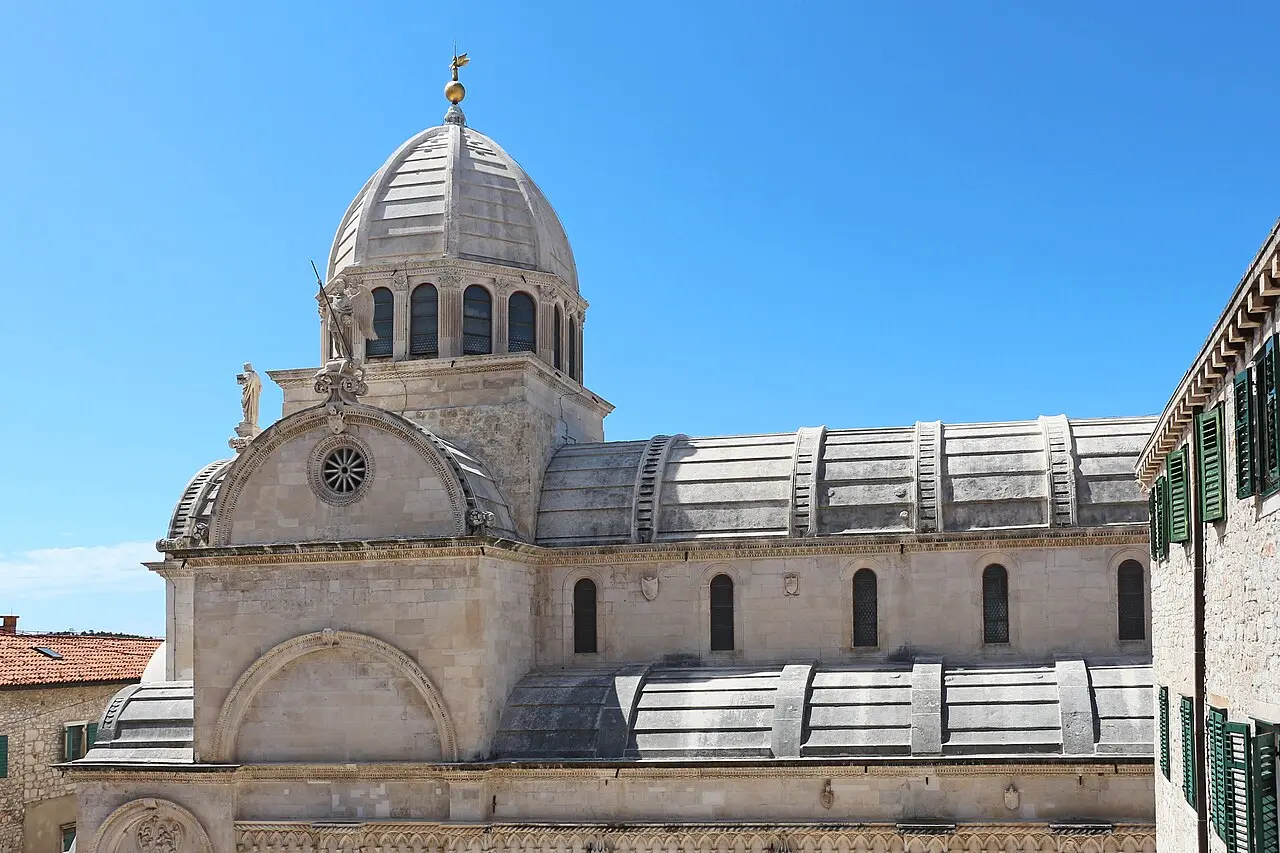 The pale ribbed stone dome and barrel-vaulted roof of the cathedral of St James in Šibenik against a blue sky