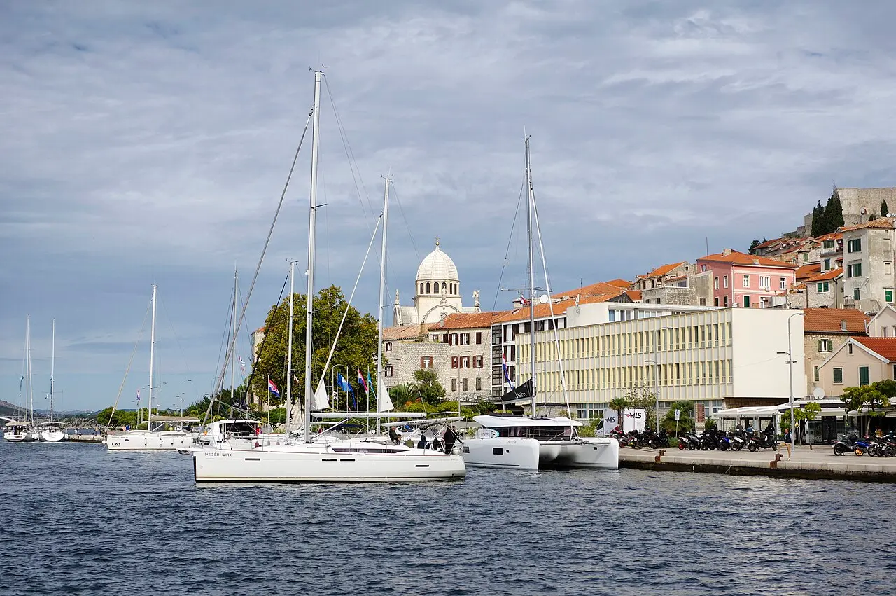 Sailing yachts moored along the Šibenik waterfront, with the pale stone dome of the cathedral rising over the old town