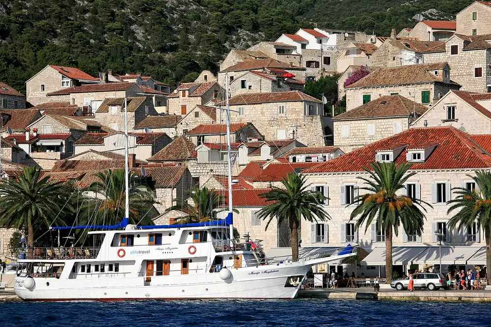 Hvar Town harbour with stone houses, palms and moored boats