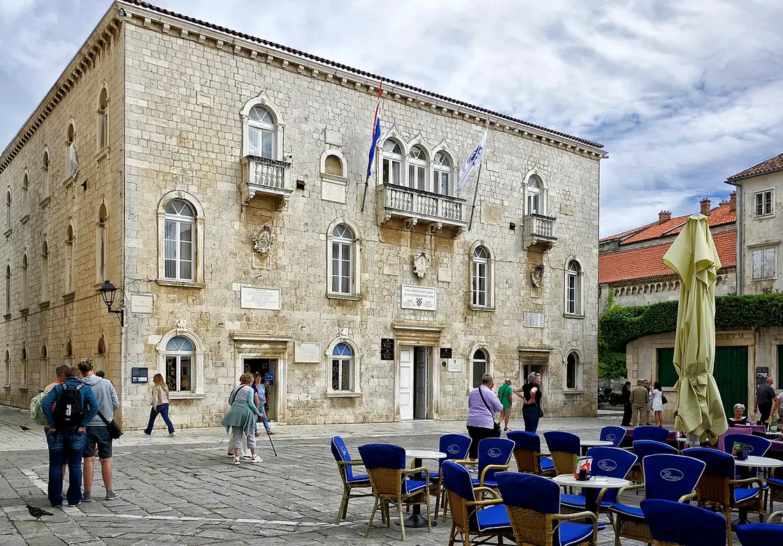 The Venetian-Gothic Čipiko Palace on the cathedral square in Trogir, with arched windows and café tables in front