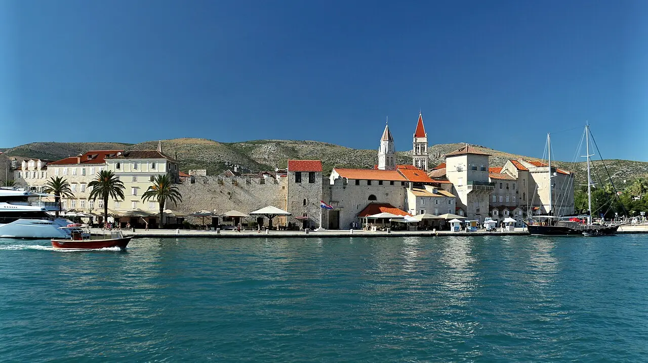 The walled island old town of Trogir seen from the water, with the cathedral bell tower rising over the palm-lined waterfront