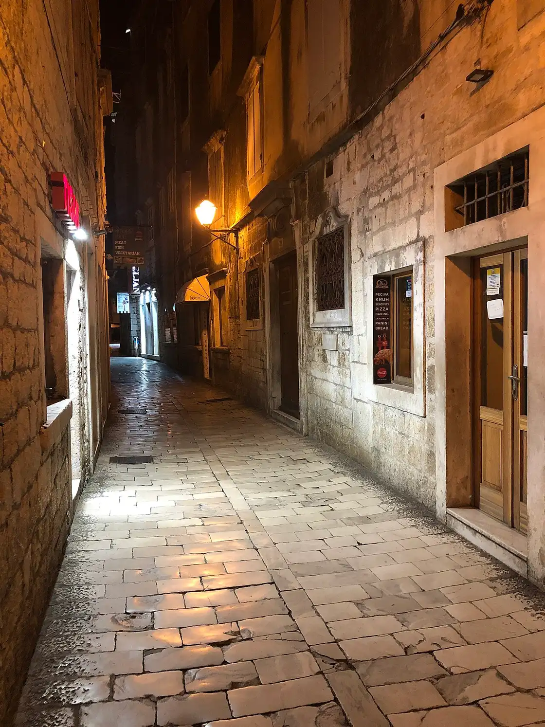 A narrow lamplit stone lane in the old town of Trogir at night, with polished paving stones and stone houses