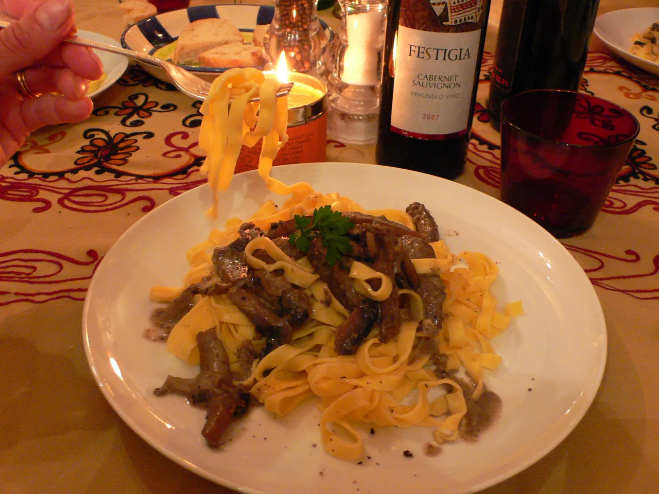 A plate of fresh Istrian pasta with truffle sauce next to a bottle of Croatian red wine by candlelight
