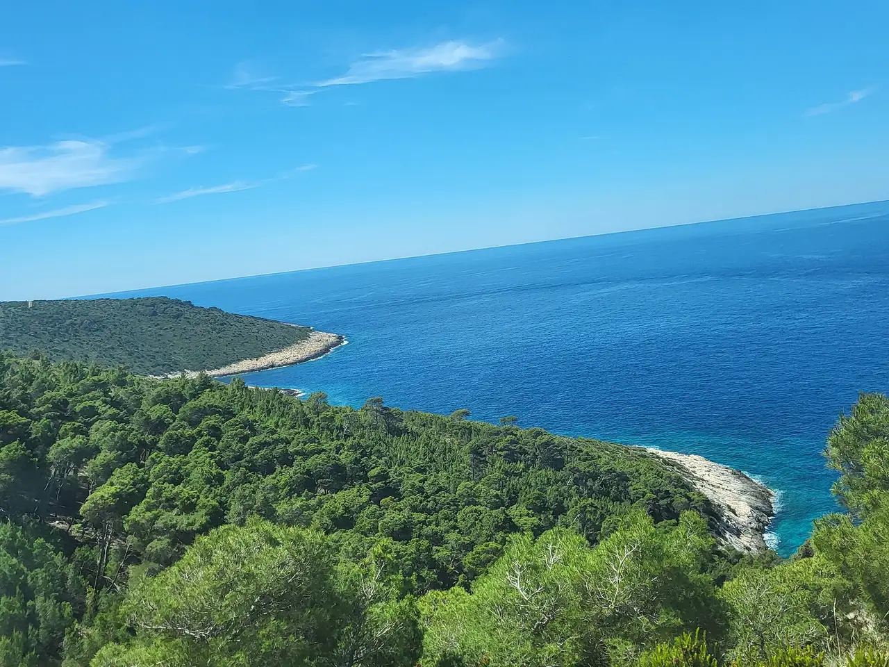 The rugged, low green island of Biševo seen across calm blue sea, ringed by rocky shore