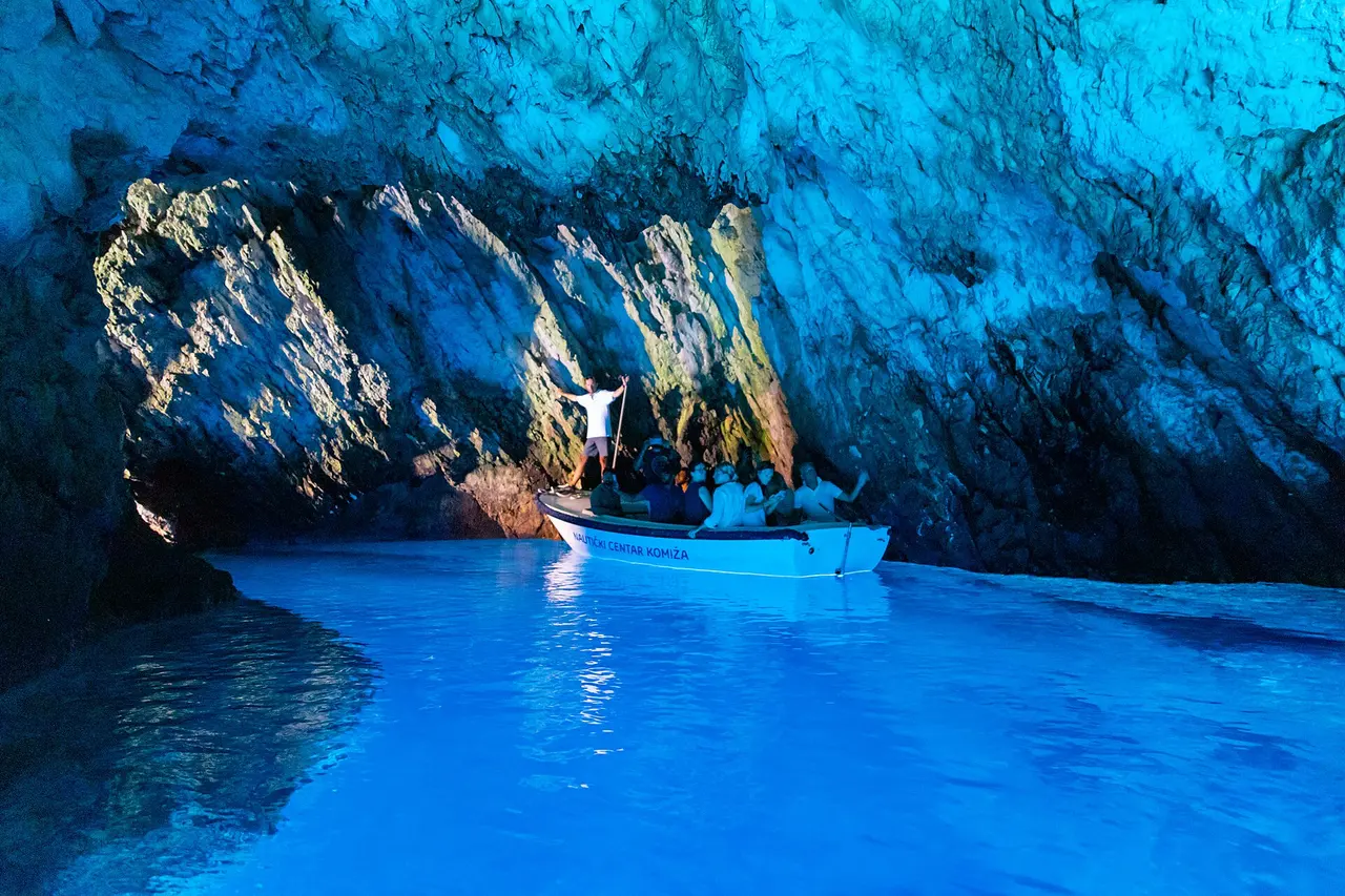 A small wooden boat full of visitors passing through the low rock entrance into the Blue Cave