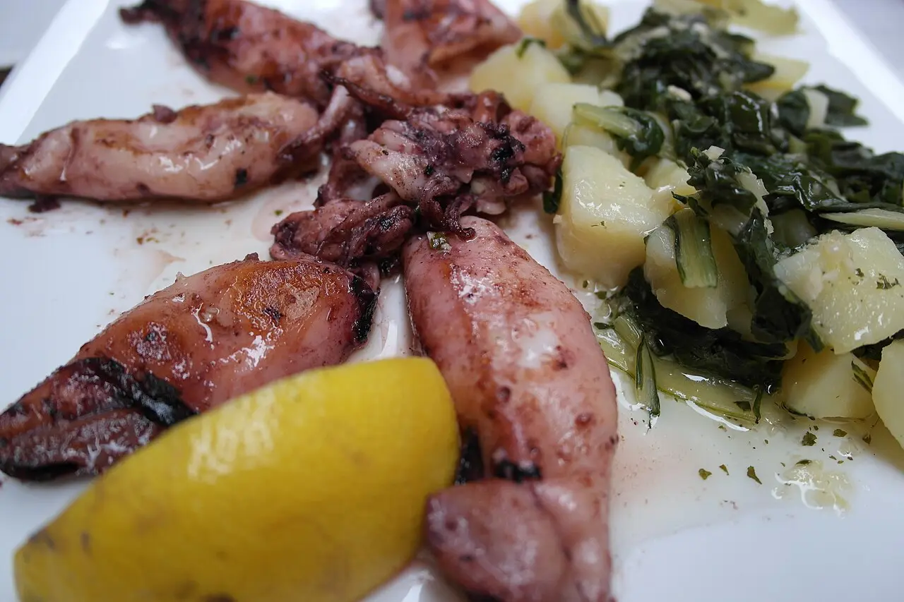 Grilled squid with lemon and blitva, chard and potato in olive oil, on a white plate