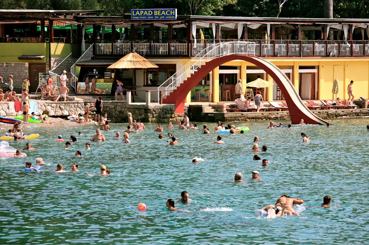 Lapad Bay pebble beach in Dubrovnik with swimmers and the wooded peninsula behind