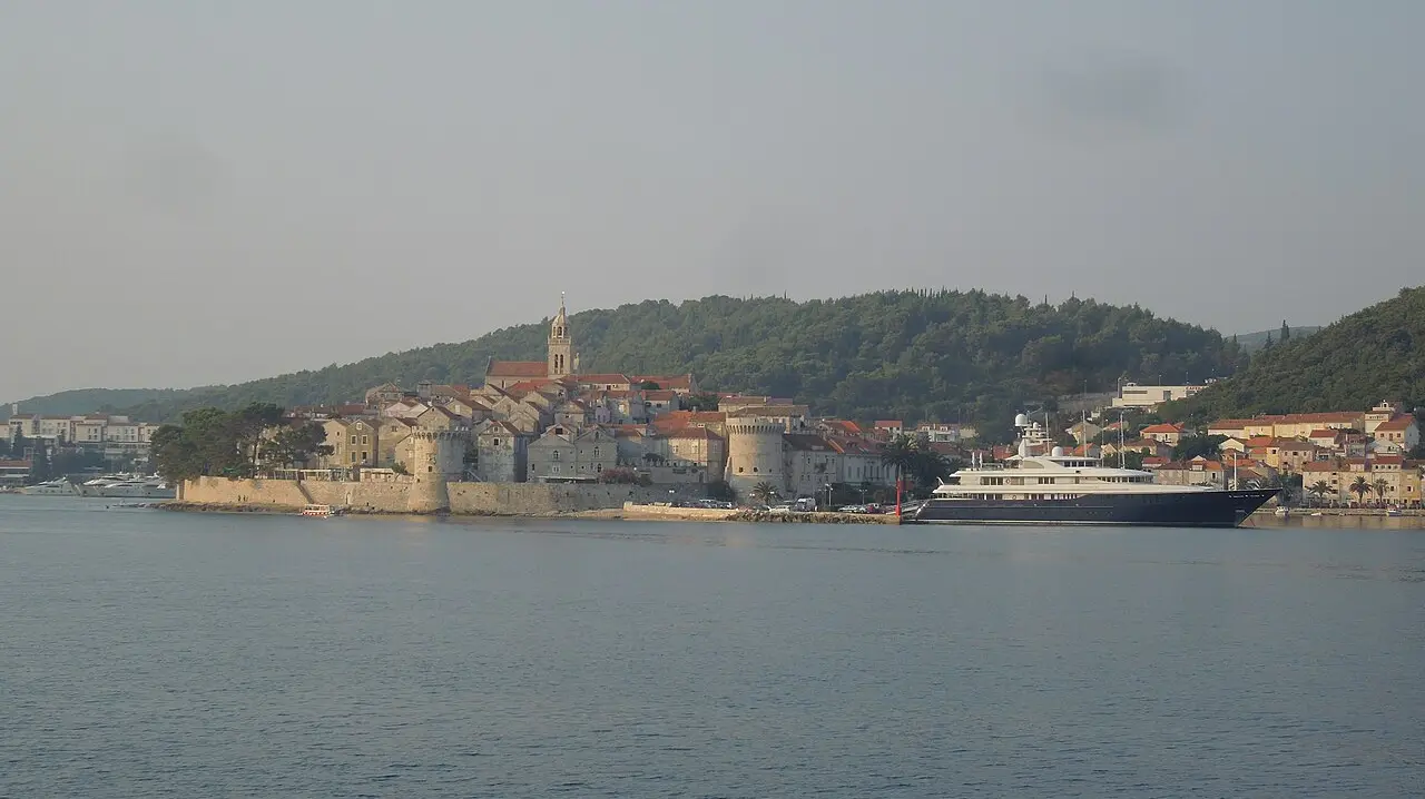 The walled old town of Korčula seen from the north across the channel, terracotta roofs and stone towers packed onto the peninsula