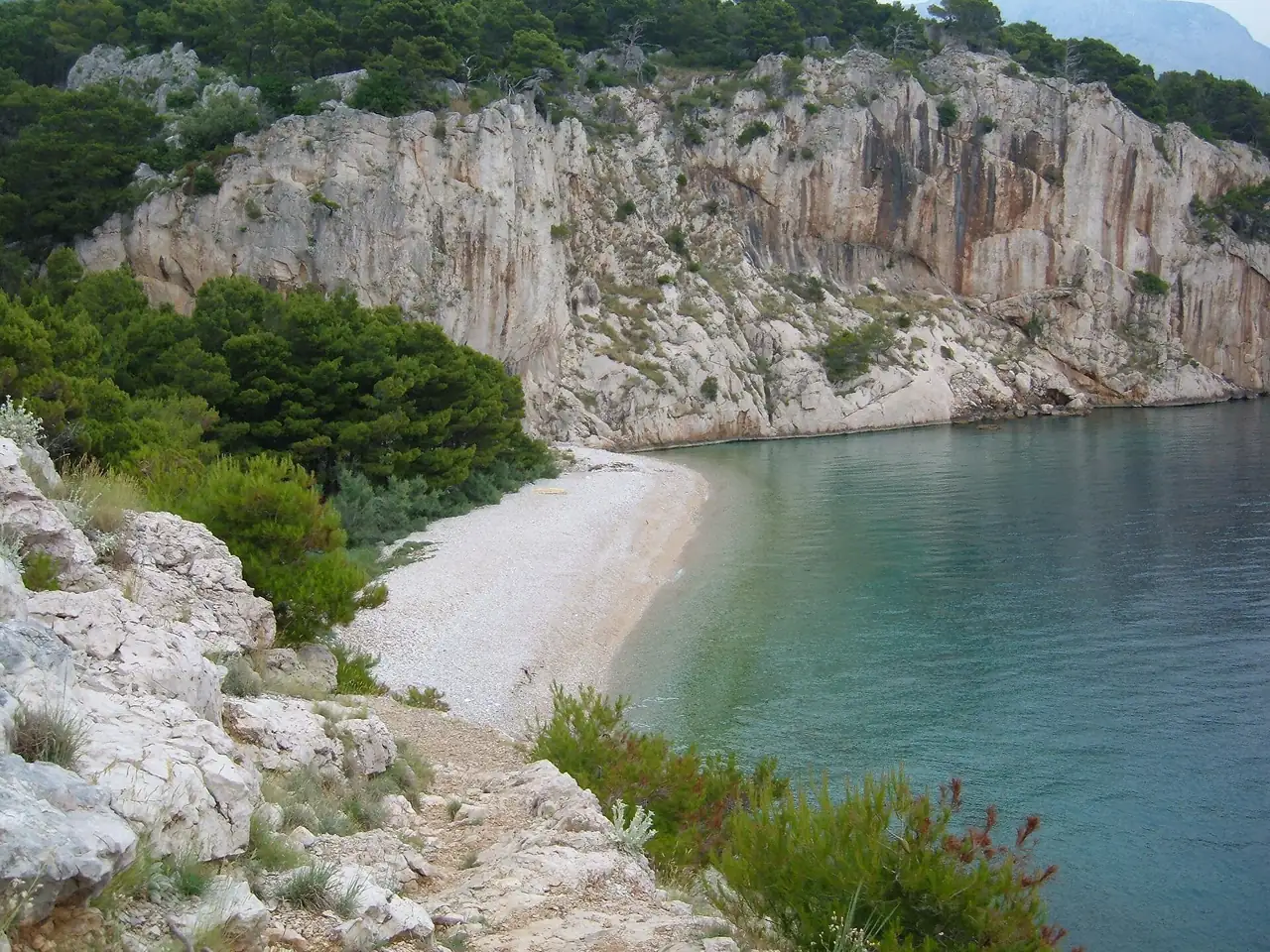 Secluded pebble cove of Nugal, a nudist beach between Makarska and Tučepi with clear water and steep cliffs, reached on foot through Osejava forest park