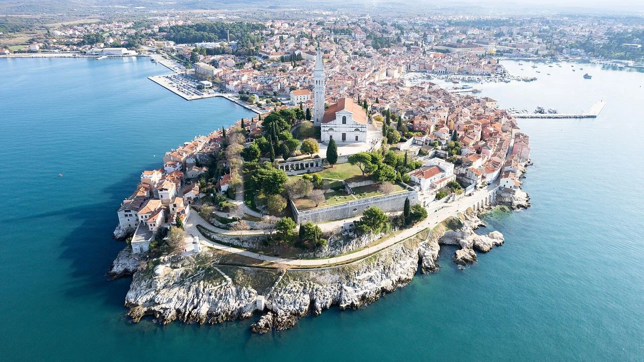 Aerial view of Rovinj old town on its peninsula, with the bell tower of St Euphemia and the wider coast and marina behind it
