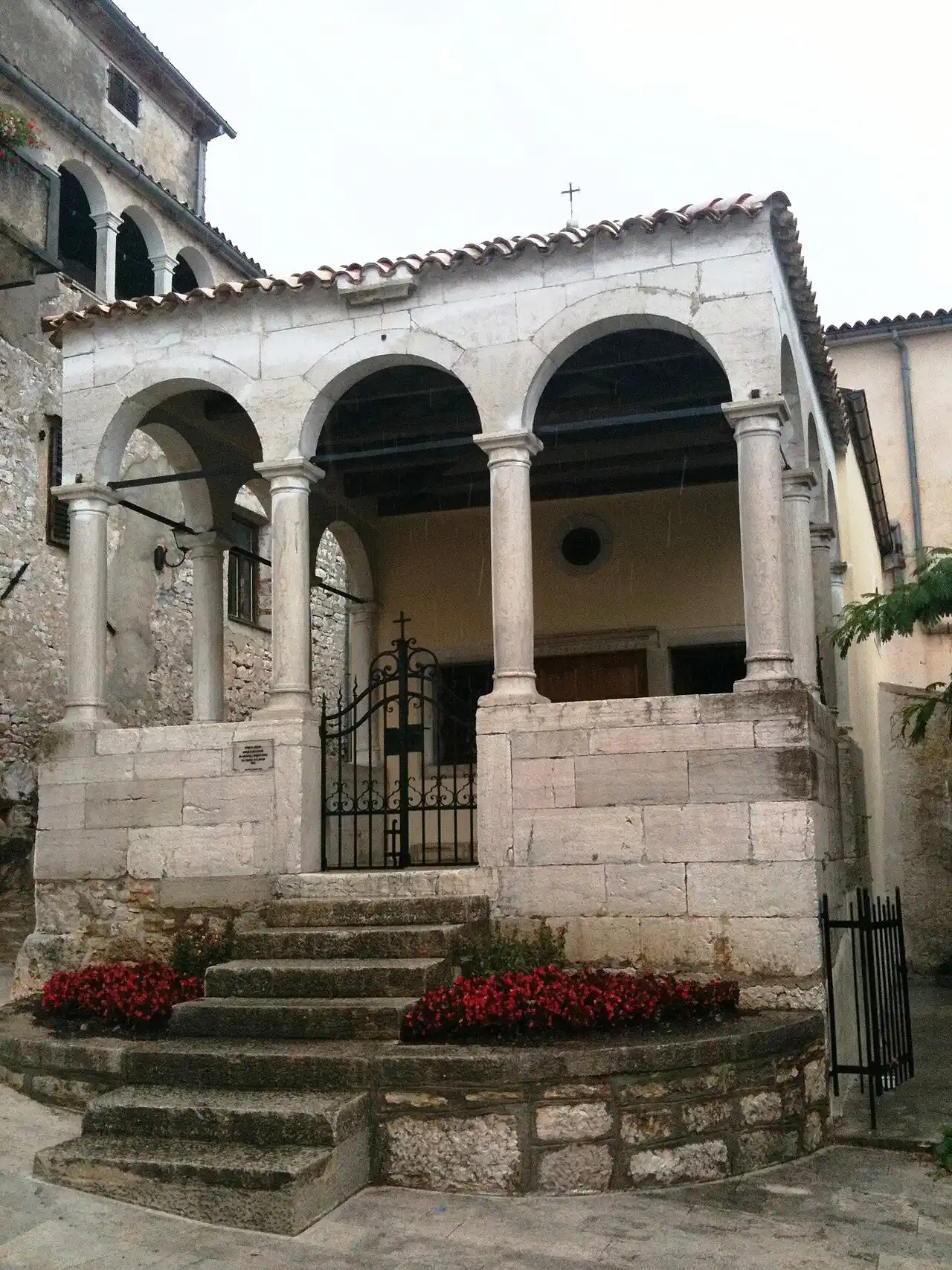 A stone stairway and arched churchyard entrance in the old town of Rovinj, with red flowers along the steps