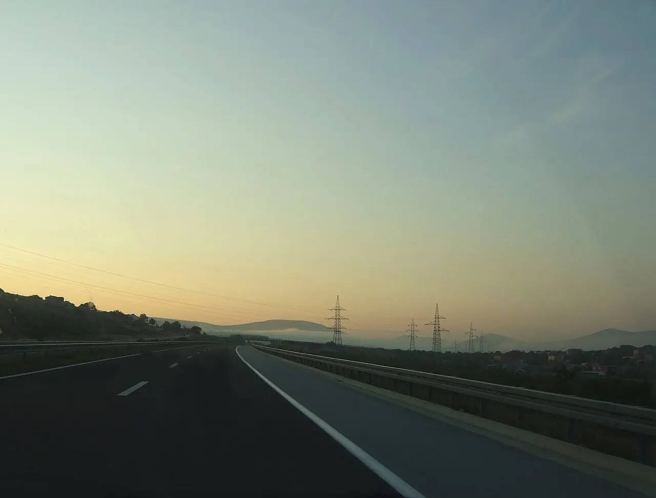 The A1 motorway running south through karst hills at dusk, with power-line pylons and mist in the valley