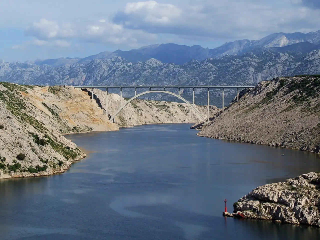 The arched Maslenica Bridge carrying the A1 motorway over a deep blue channel between karst cliffs, with the Velebit mountains behind