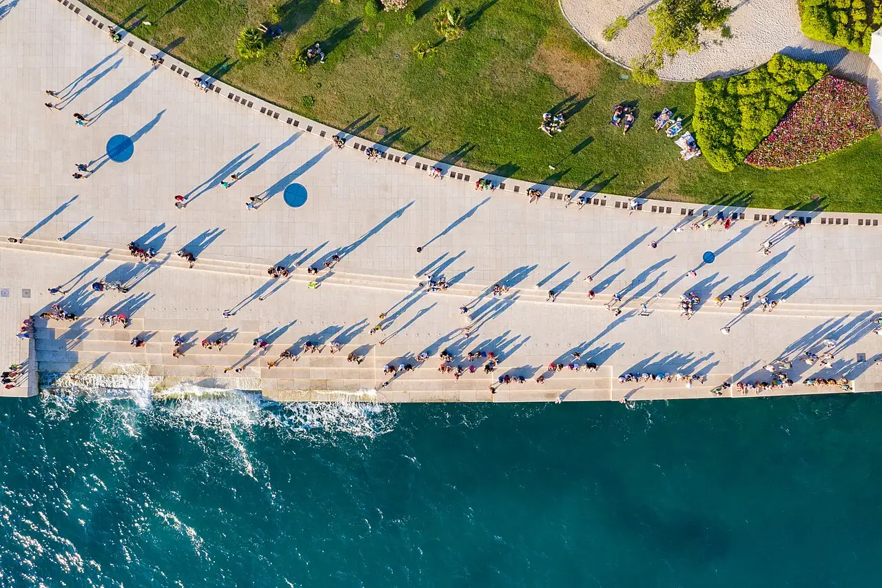 Aerial view of Zadar's Sea Organ steps meeting the Adriatic, with people walking along the promenade