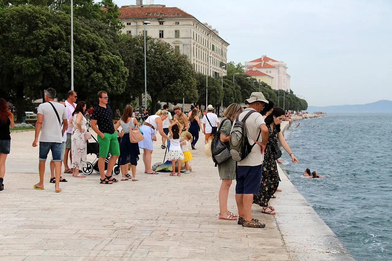 People strolling along Zadar's marble Riva promenade beside the sea, with the old town buildings behind