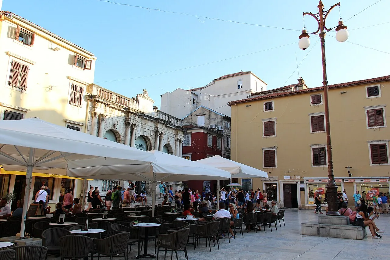 People crossing the paved Narodni trg (People's Square) in Zadar, framed by the Renaissance City Loggia and Town Guard
