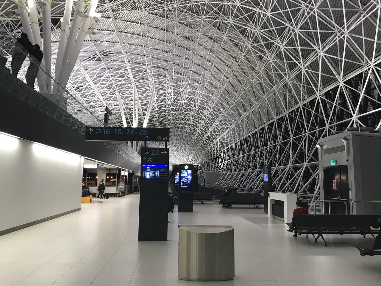The white steel-lattice roof over the gate concourse at Zagreb Airport, with gate signs and a departures board
