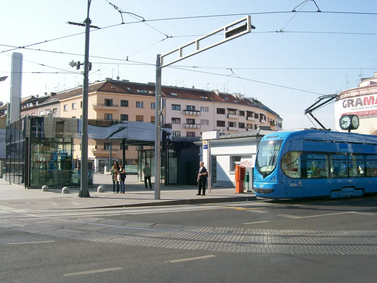 Kvaternik Square in Zagreb with a blue ZET tram arriving beside a glass kiosk building and apartment blocks