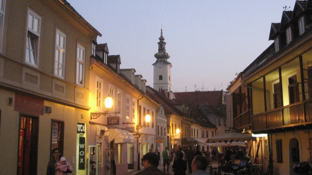Tkalčićeva street in Zagreb at dusk, its lit terraces filling with people below the floodlit church tower