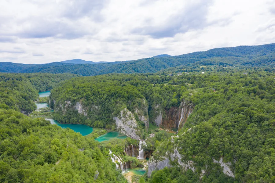 Aerial view of the Great Waterfall and the turquoise lower lakes at Plitvice in dense forest