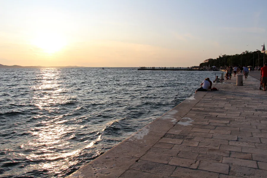 Sunset over the Adriatic from the stone waterfront promenade in Zadar with people on the pier